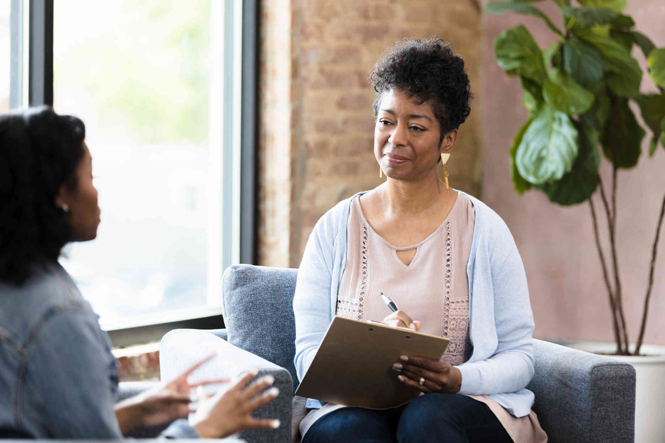 A female therapist quietly takes notes as she listens to the female patient sitting infront of her talk during a therapy session.